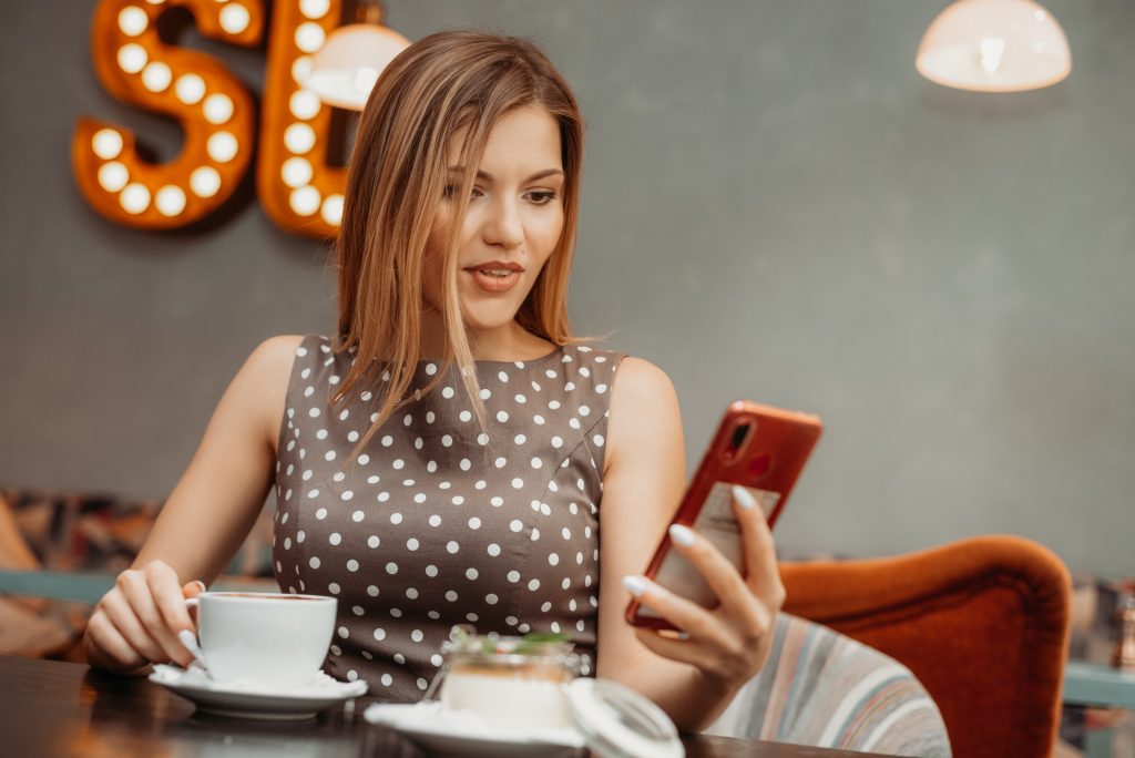 Beautiful relaxed woman using a mobile phone in cafe. Reading news or SMS